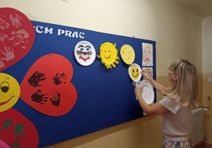 Pani Kasia przypina wykonane prace dzieci i rodziców na tablicy.