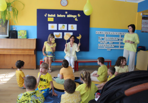Żółty dzień w przedszkolu - przedszkolaki siedzą na dywanie, słychają piosenki śpiewanej przez p. Kasię i Kingę