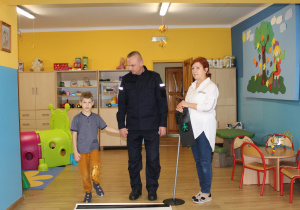 Miłosz z funkcjonariuszem Policji podczas ćwiczeń przechodzenia przez jezdnię (ćwiczenia w sali)