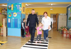 Ania z panią Ulą i funkcjonariuszem Policji podczas ćwiczeń przechodzenia przez jezdnię (ćwiczenia w sali)