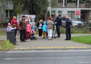 Przedszkolaki podczas przechodzenia przez ulicę pod opieką funkcjonariusza Policji i wychowawców