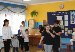 Natalia pod opieką p. Moniki recytuje wierszyk, w tle pozostałe przedszkolaki i panie