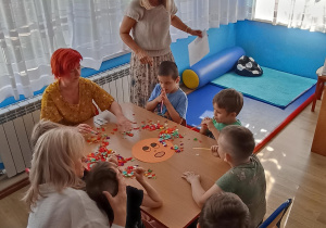 Dzieci z grupy 3 rozdmuchują przez słomki bibułę z emotki przedstawiającej strach.