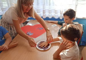 Dzieci z grupy 1 odbijają swoje dłonie na czerwonym sercu.