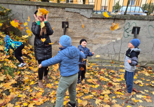 Jesienne zabawy na świeżym powietrzu - na zdjęciu przedszkolaki wraz z paniami obrzucają się liśćmi