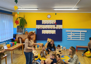 Dzieci ze swoimi misiami siedzą na dywanie.