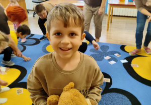 Na pierwszym planie Boguś z misiem, w tle dzieci szukają misiów.