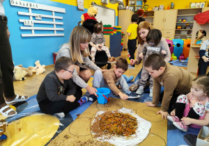 Dzieci wyklejają misia różnymi materiałami.