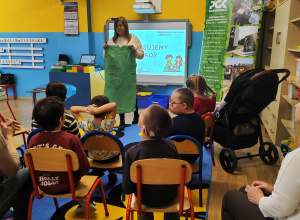 Pani z PGK prezentuje dzieciom zielony worek na szkło.